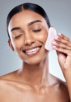 Buy stock photo Beauty, smile and gua sha with face of woman in studio for massage, wellness and cosmetics. Spa, self care and glow with model on grey background for facial, cosmetology and rose quartz crystal