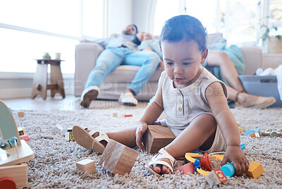 Buy stock photo Shot of a little girl playing on the floor while her parents nap in the background