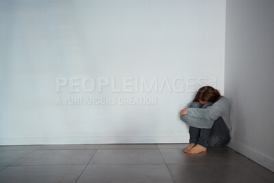 Buy stock photo Shot of a depressed young woman sitting in a corner alone