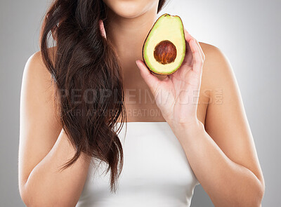 Buy stock photo Studio cropped shot of an unrecognizable woman holding an avocado while posing against a grey background