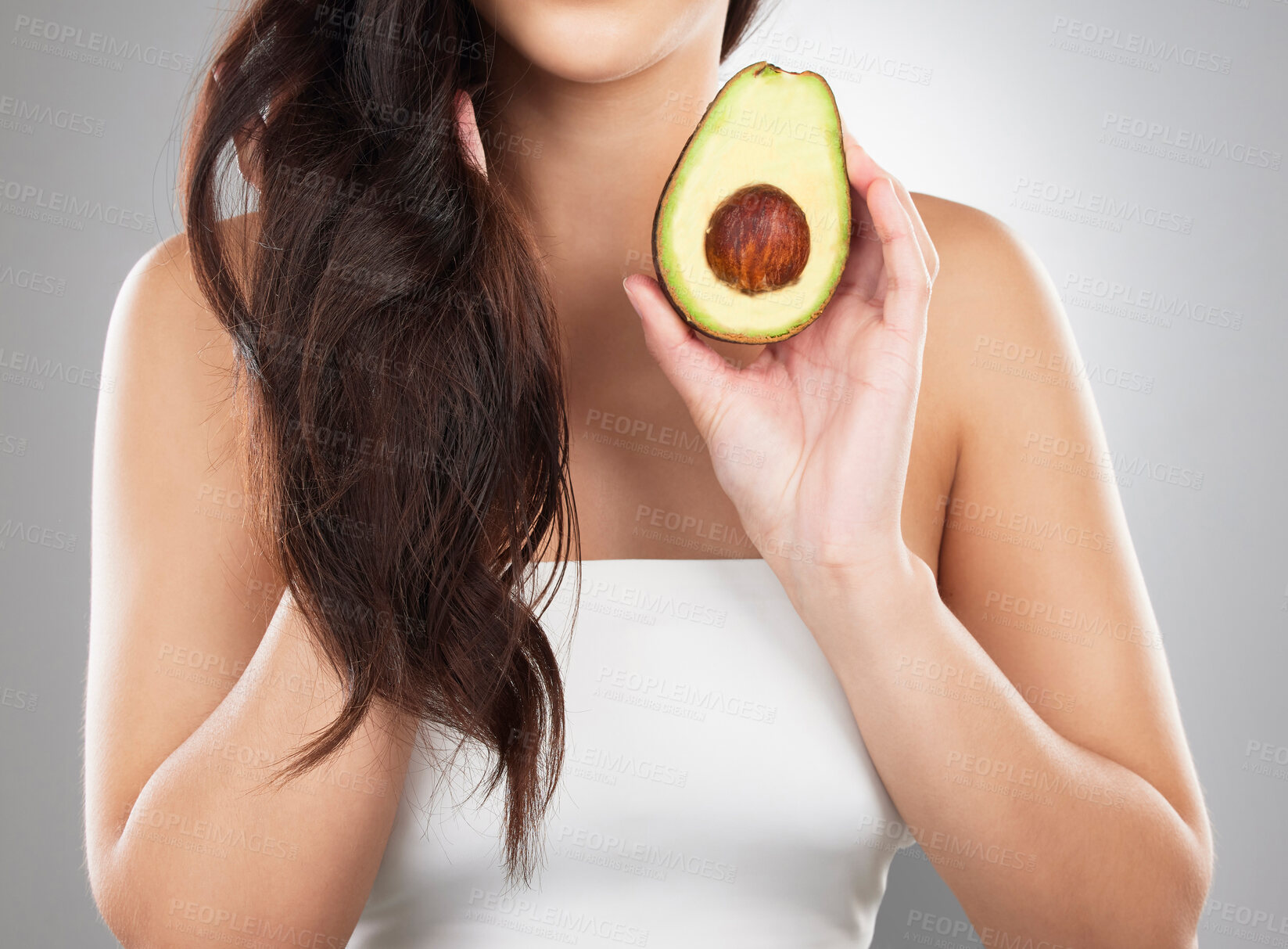 Buy stock photo Hair care, wellness and woman with an avocado in a studio for a natural, organic or health mask. Self care, beauty and closeup of a female model with a fruit for a hair treatment by a gray background