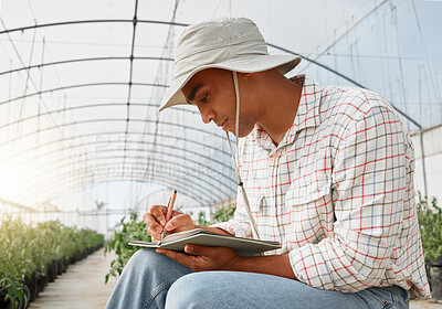 Buy stock photo Shot of a young man writing notes while working in a greenhouse on a farm