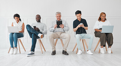 Buy stock photo Shot of a diverse group of people using digital devices while sitting in line against a white background