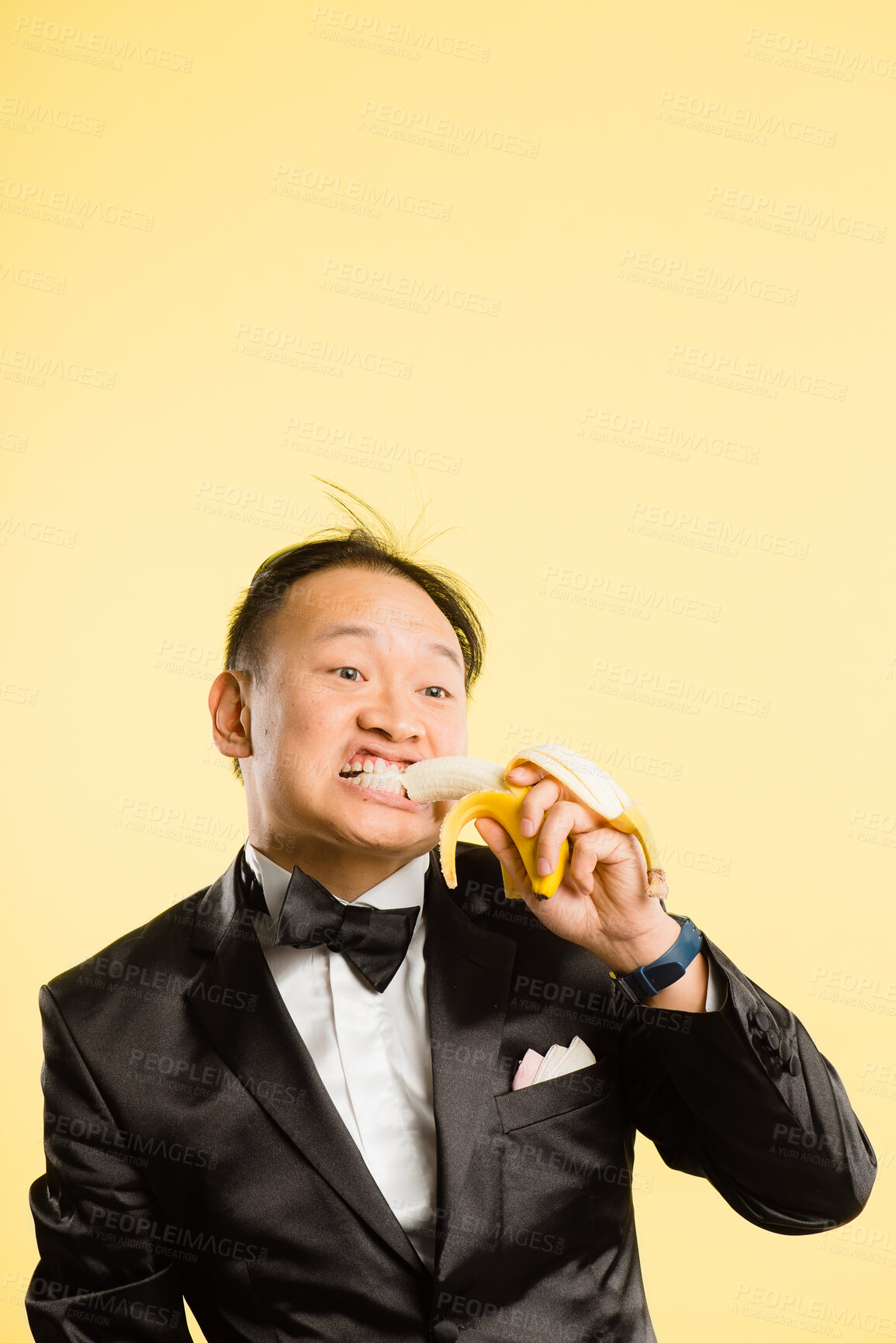 Buy stock photo Man, tuxedo and eating banana in studio with funny face, bite and playful with fashion by background. Chinese person, fruit and comic with mockup space for diet, food and nutrition with monkey suit