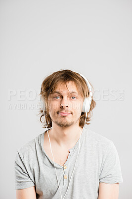 Buy stock photo Shot of a handsome young man sitting alone in the studio and listening to music through headphones