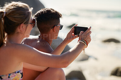 Buy stock photo Shot of a couple taking selfies while relaxing at the beach