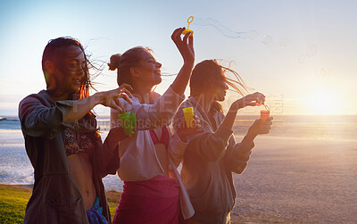 Buy stock photo Women, friends and bubbles at beach, sunset and happy on vacation with game, bonding and playful in summer. Girl, group and plastic container with smile, foam and liquid on holiday by sea in Portugal