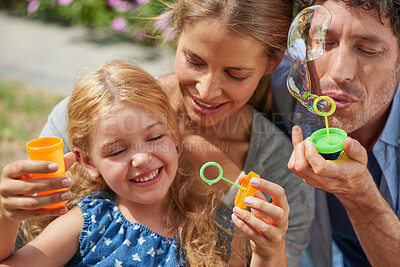 Buy stock photo Parents, girl child and bubbles in backyard with bonding, relax and playful with smile for memory. Father, mother and daughter with soap, liquid and teaching with connection, care and love in Germany