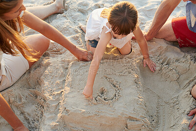 Buy stock photo Parents, girl and vacation at beach with sandcastle, play or bonding for family, love and above for heart icon. Father, mother and daughter with care, building and game for drawing on ground in Spain