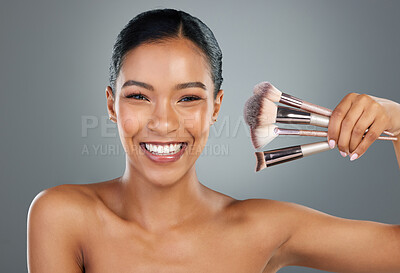 Buy stock photo Happy woman, portrait and beauty with makeup brushes for cosmetics or facial on a gray studio background. Young, female person or model with smile, utensils or tools for beautician or makeover