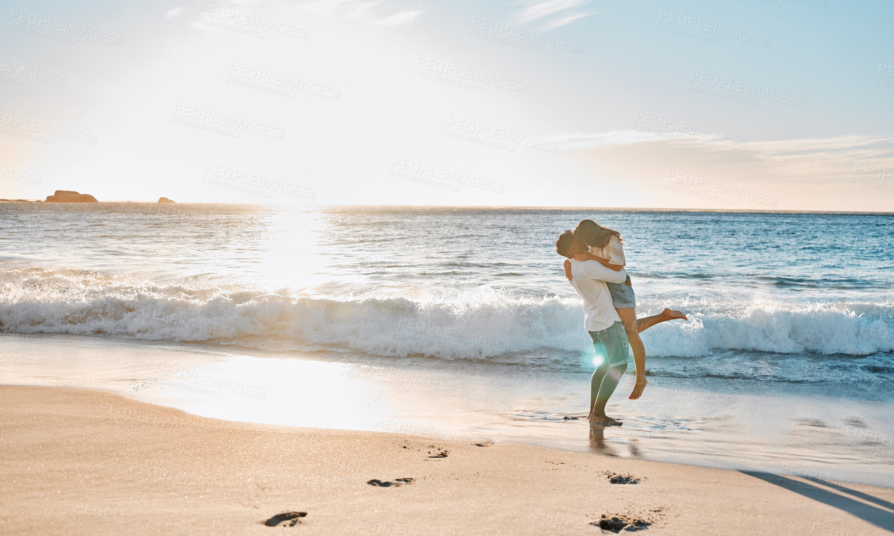 Buy stock photo Sunset, couple and kiss with lifting on beach, travel vacation and anniversary holiday for bonding. Summer, man and woman on ocean for carrying, love connection and healthy relationship by seaside