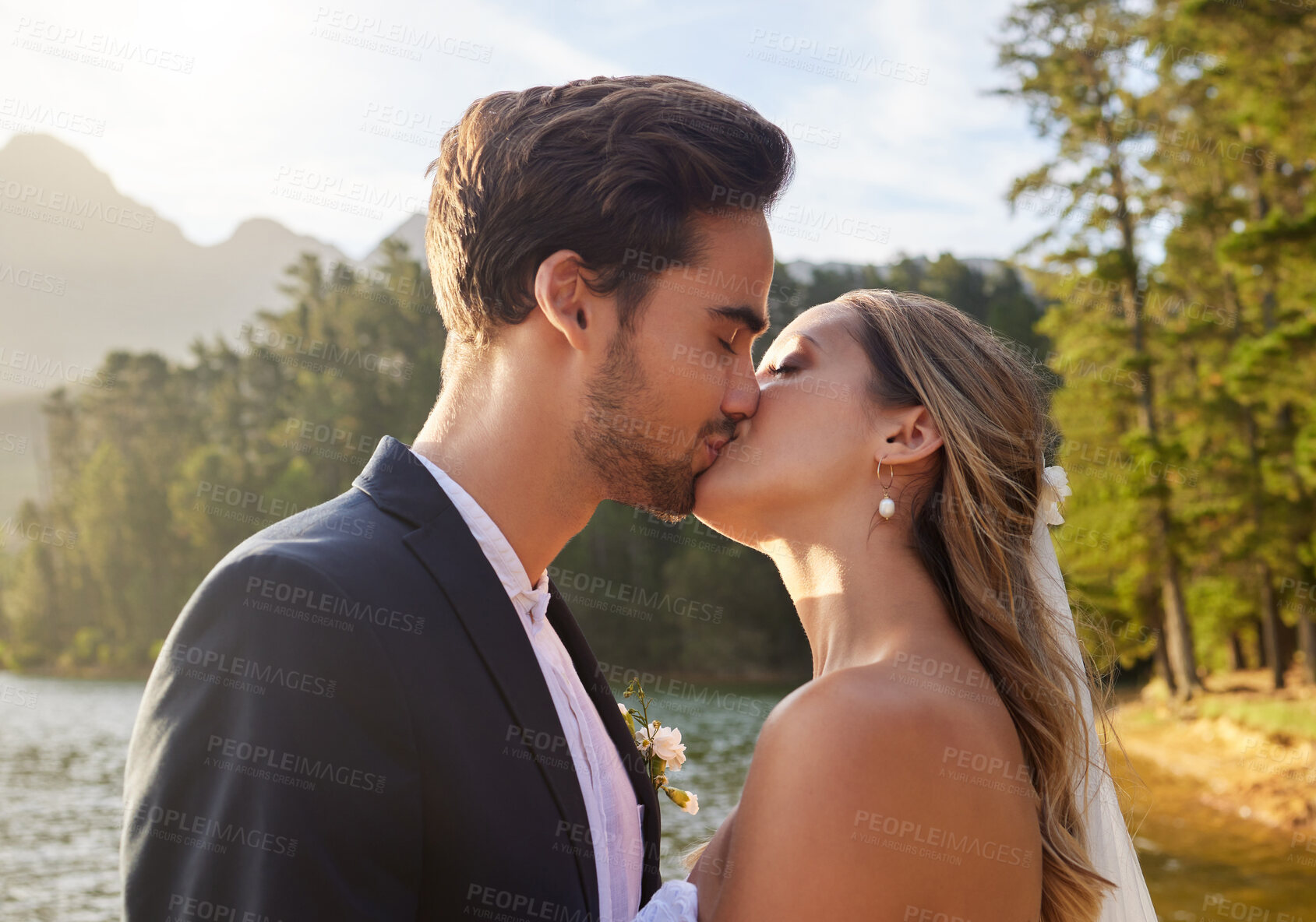 Buy stock photo Love, wedding and kiss with a newlywed couple by a lake outdoor in celebration of marriage or romance. Water, summer and a bride and groom kissing while bonding together in tradition after ceremony