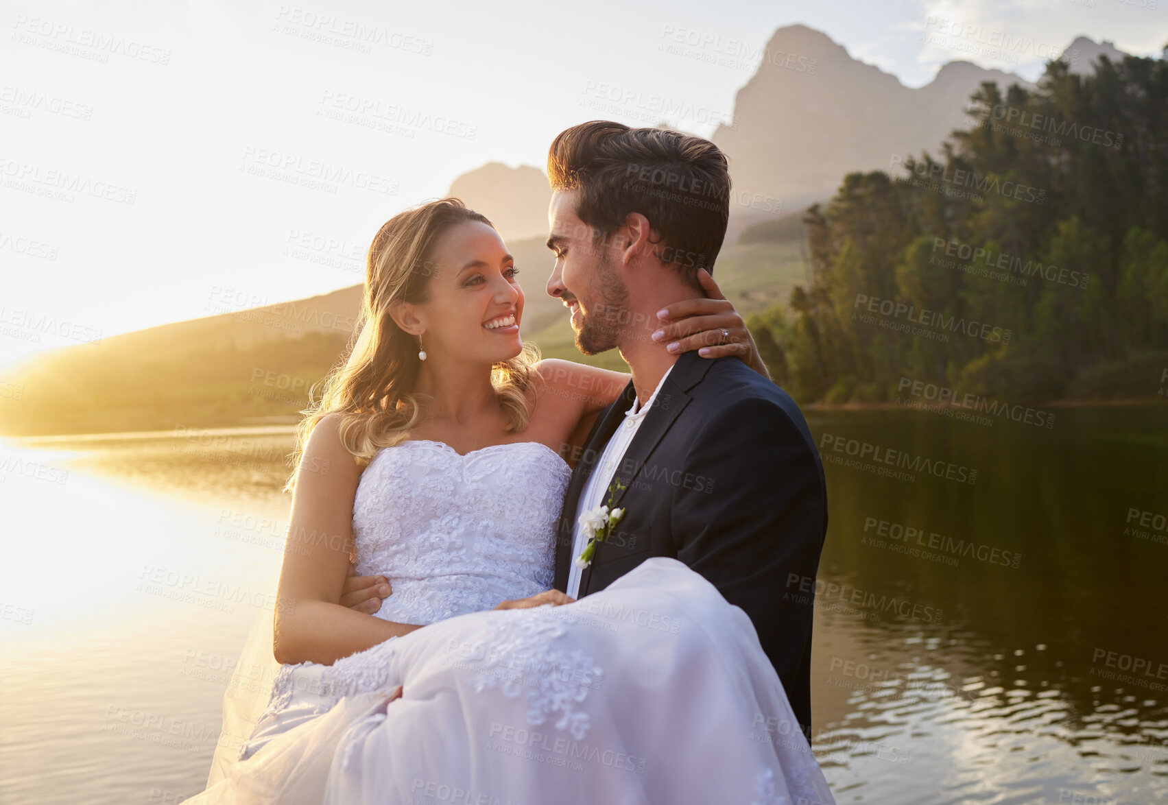 Buy stock photo Lake, wedding and man carrying his bride while having an intimate moment together in nature. Happiness, love and young couple with affection on their romantic outdoor marriage day ceremony by forest.