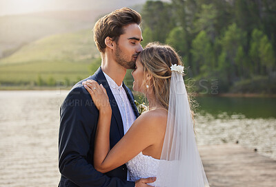 Buy stock photo Couple, wedding and forehead kiss by lake on romantic honeymoon or getaway together in nature. Man kissing woman on head and hugging for marriage, relationship or loving embrace in the outdoors