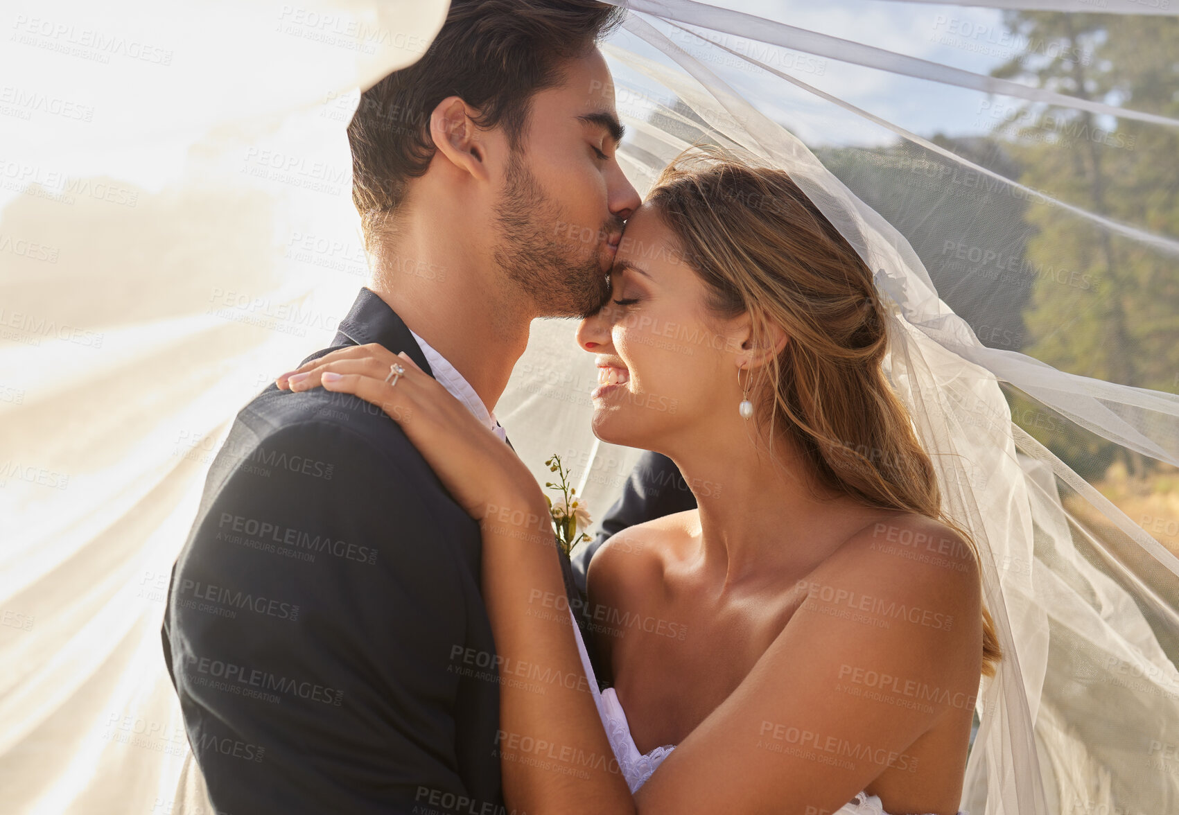 Buy stock photo Couple, wedding and forehead kiss with vail for love, compassion or affection together in nature. Marred man kissing woman on head and hugging in marriage, relationship or loving embrace outdoors