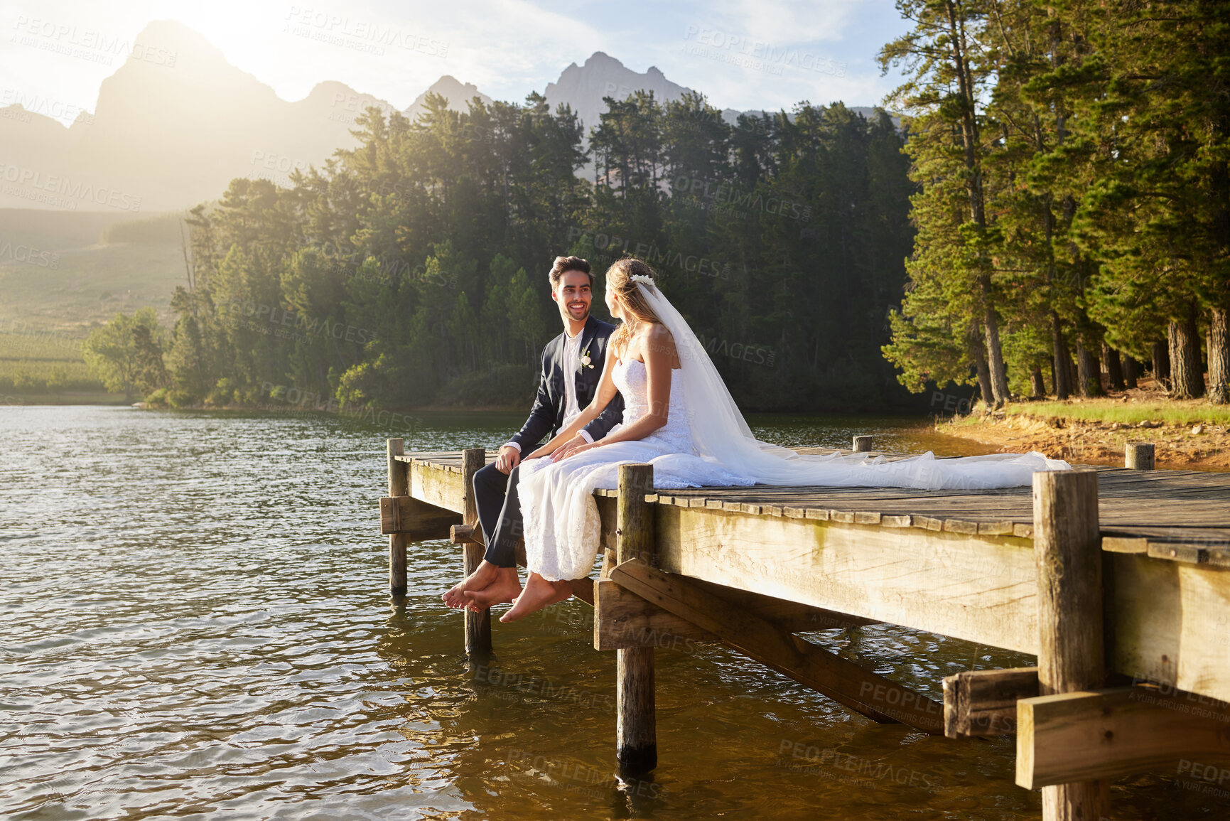 Buy stock photo Forest, lake and a married couple on a pier in celebration together after a wedding ceremony of tradition. Marriage, love or romance with a bride and groom sitting outdoor while bonding in nature