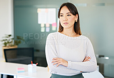 Buy stock photo Shot of an attractive young businesswoman standing alone in the office with her arms folded and looking contemplative