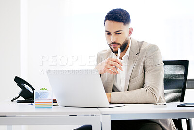 Buy stock photo Shot of a handsome young businessman sitting alone in the office and looking contemplative while using his laptop