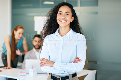 Buy stock photo Shot of an attractive young businesswoman standing in the office with her arms folded while her colleagues work behind her