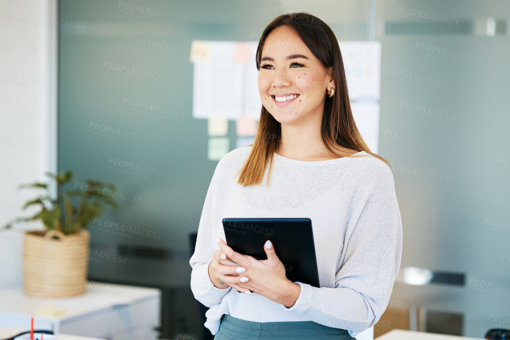 Buy stock photo Shot of an attractive young businesswoman standing alone in the office and holding a digital tablet