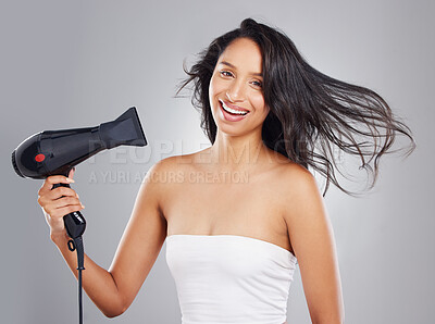 Buy stock photo Cropped portrait of an attractive young woman blowdrying her hair against a grey background