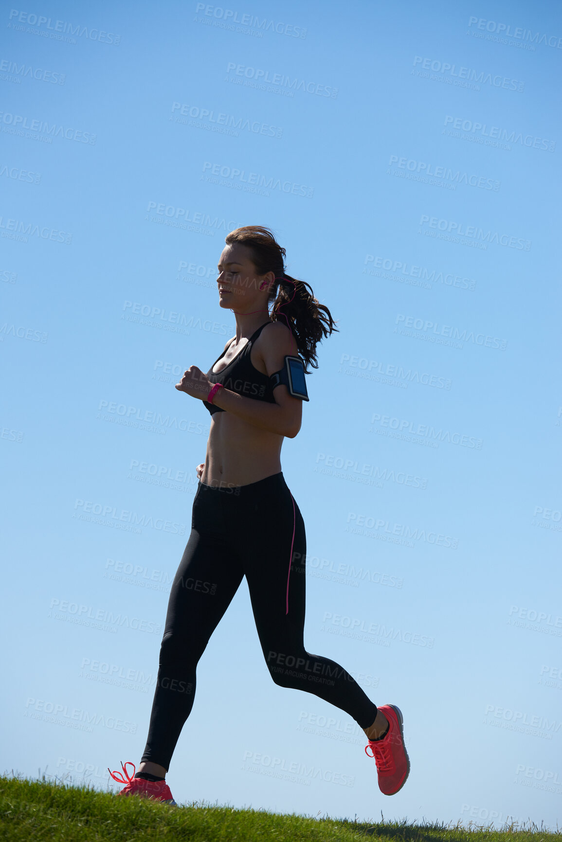 Buy stock photo Woman runner, grass and sky for fitness, health and wellness in summer, sunshine or outdoor. Athlete girl, running and workout with tech, phone or exercise for speed, self care or healthy strong body