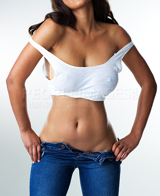 Buy stock photo Studio portrait of a sexy young woman smiling while taking off her jeans against a grey background