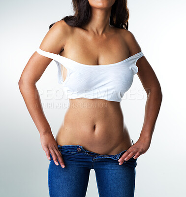 Buy stock photo Studio portrait of a sexy young woman smiling while taking off her jeans against a grey background