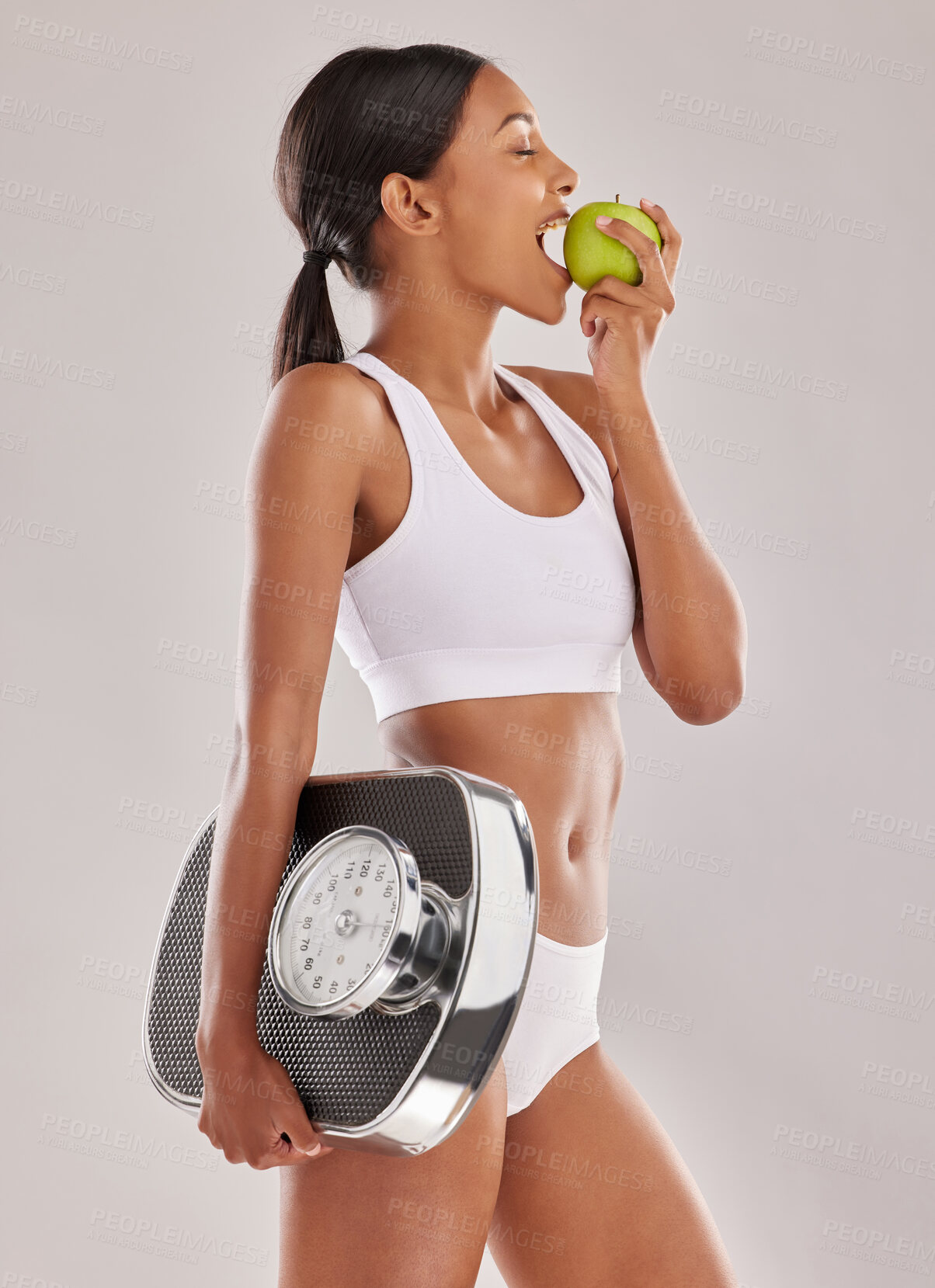 Buy stock photo Studio shot of a young woman eating an apple and holding a weight scale