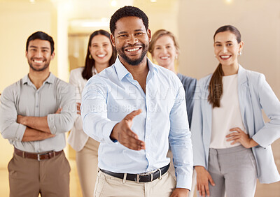 Buy stock photo Portrait of a young businessman extending a handshake in an office with his colleagues in the background