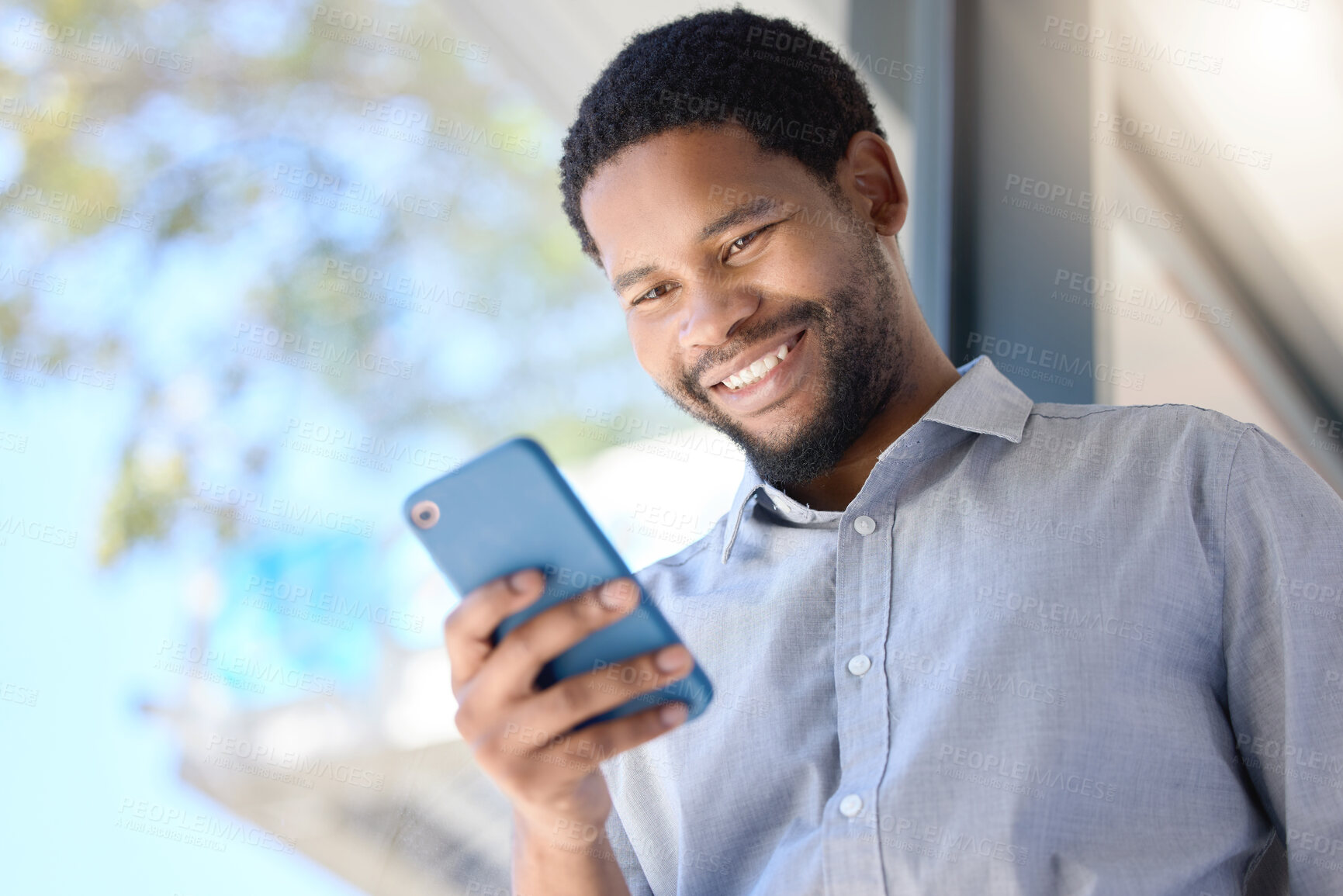 Buy stock photo Black man, typing and reading with phone by window for communication, social media or news at office. Happy businessman, employee or smile on mobile smartphone for online chat or texting at workplace