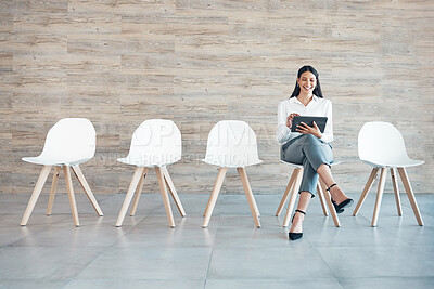 Buy stock photo Full length shot of an attractive young businesswoman sitting alone in the office and using a digital tablet