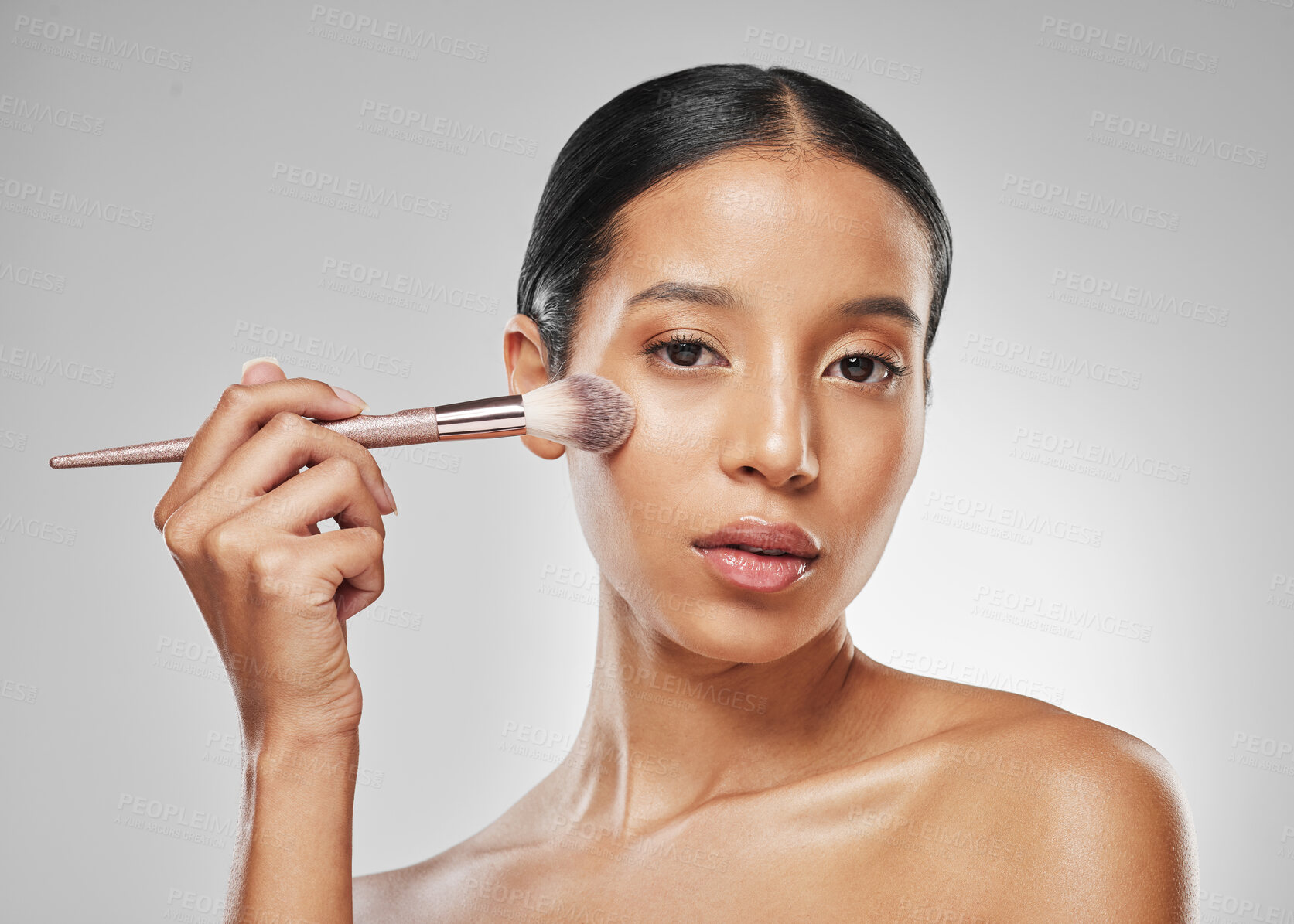 Buy stock photo Studio portrait of an attractive young woman applying makeup to her face with a brush against a grey background