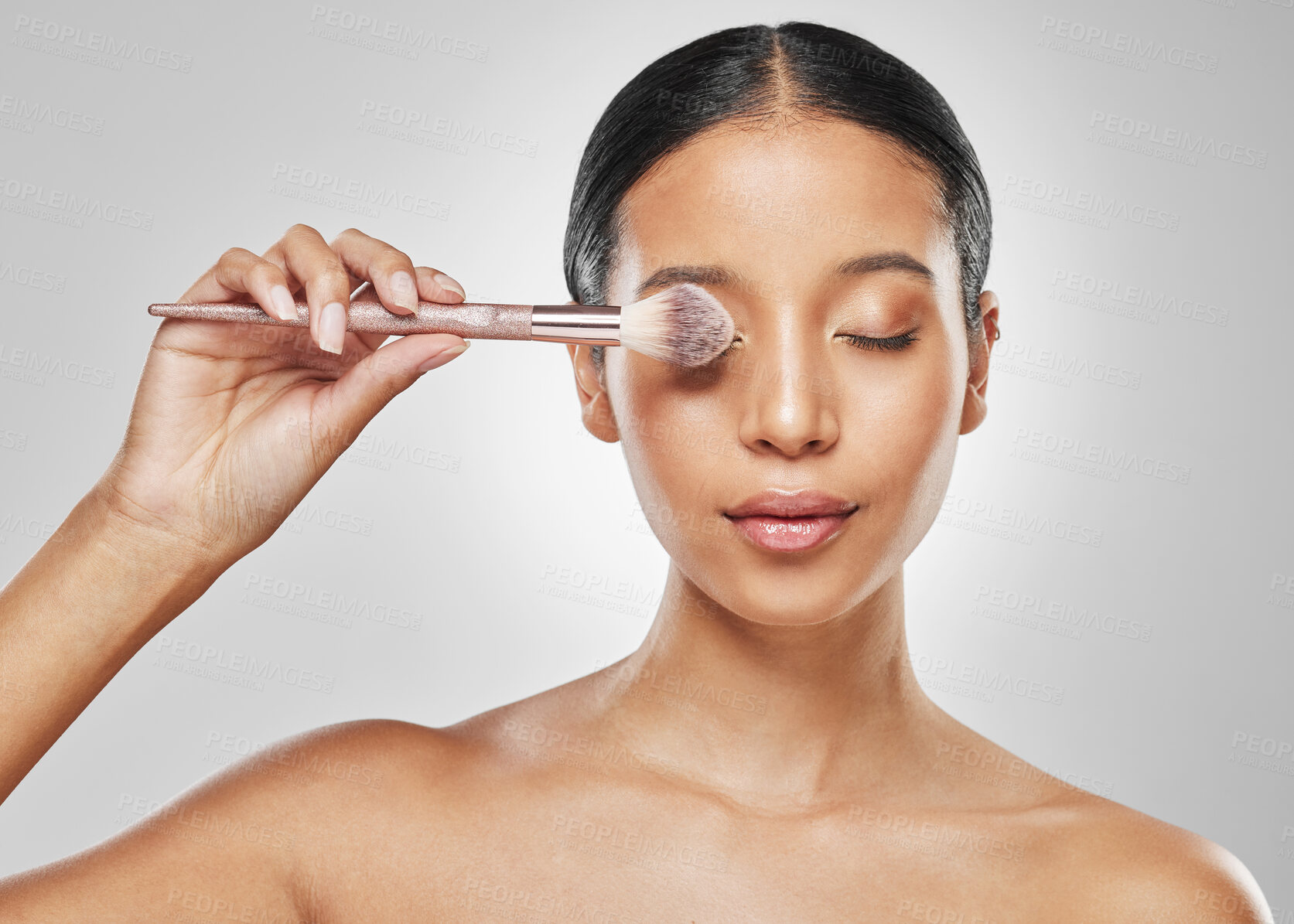 Buy stock photo Studio shot of an attractive young woman posing with a makeup brush against a grey background