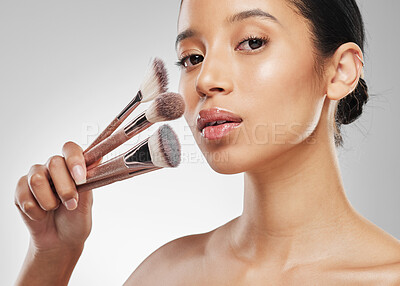 Buy stock photo Studio portrait of an attractive young woman holding a collection of makeup brushes against a grey background