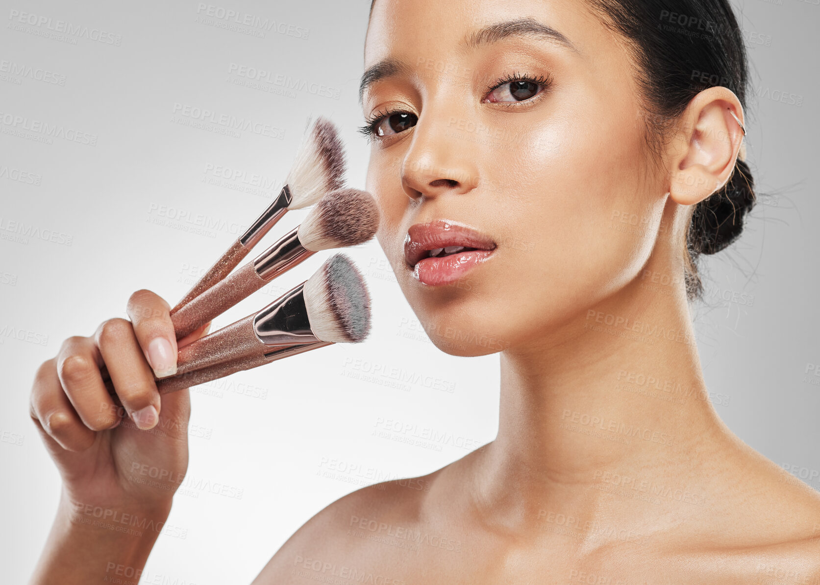 Buy stock photo Studio portrait of an attractive young woman holding a collection of makeup brushes against a grey background