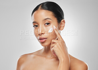 Buy stock photo Studio portrait of an attractive young woman applying moisturiser on her face against a grey background