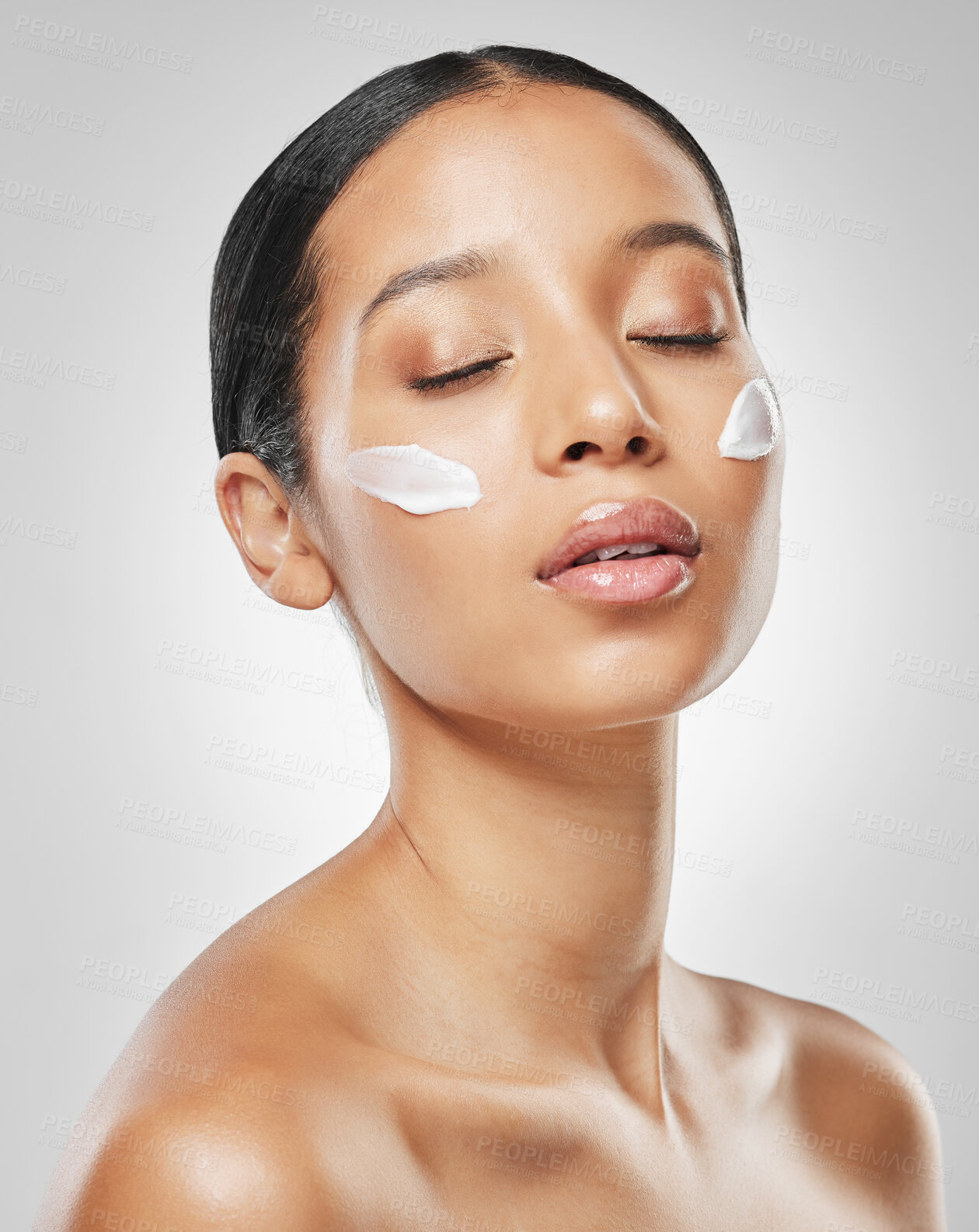 Buy stock photo Studio shot of an attractive young woman posing with moisturiser on her face against a grey background