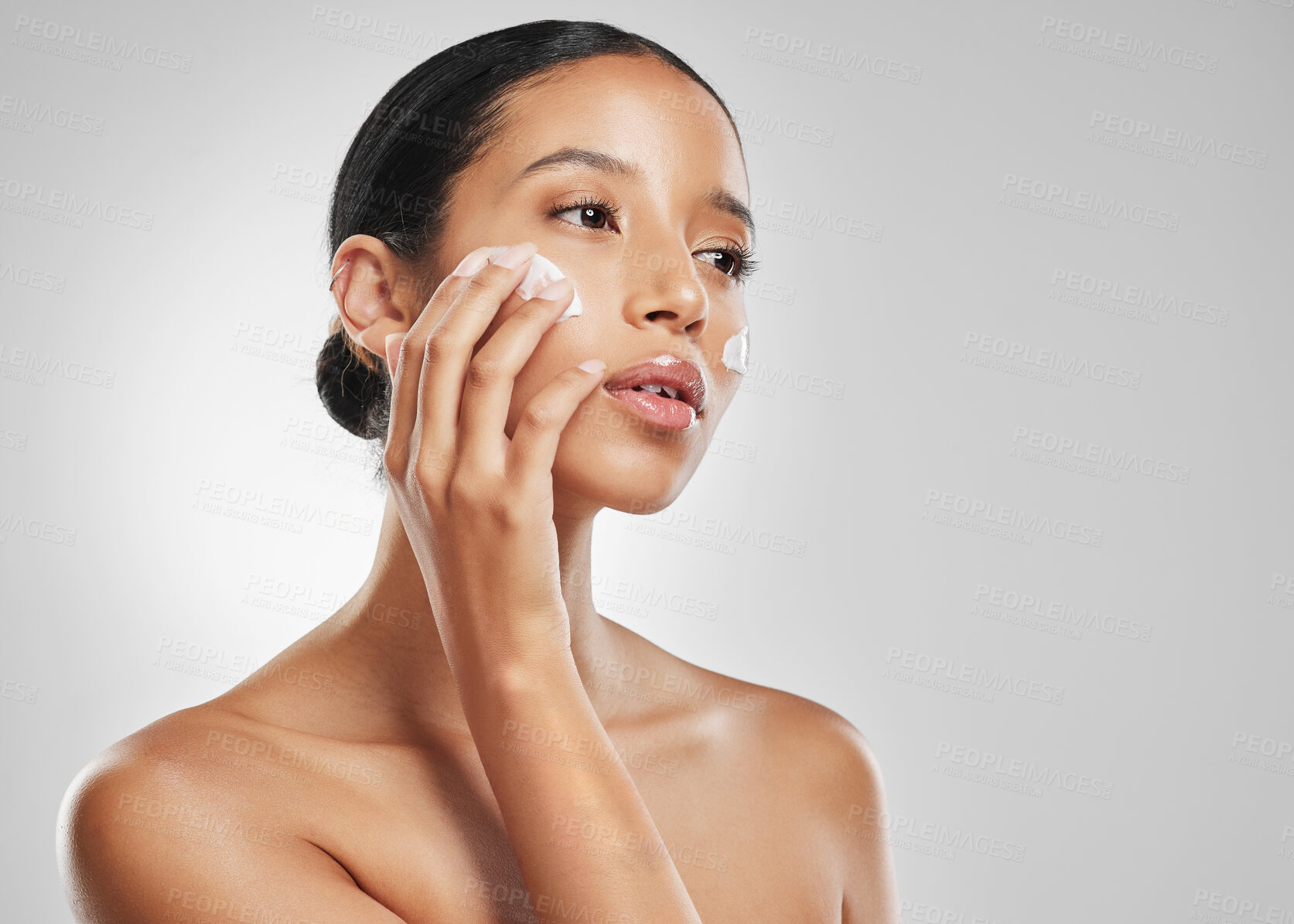 Buy stock photo Studio shot of an attractive young woman applying moisturiser on her face against a grey background