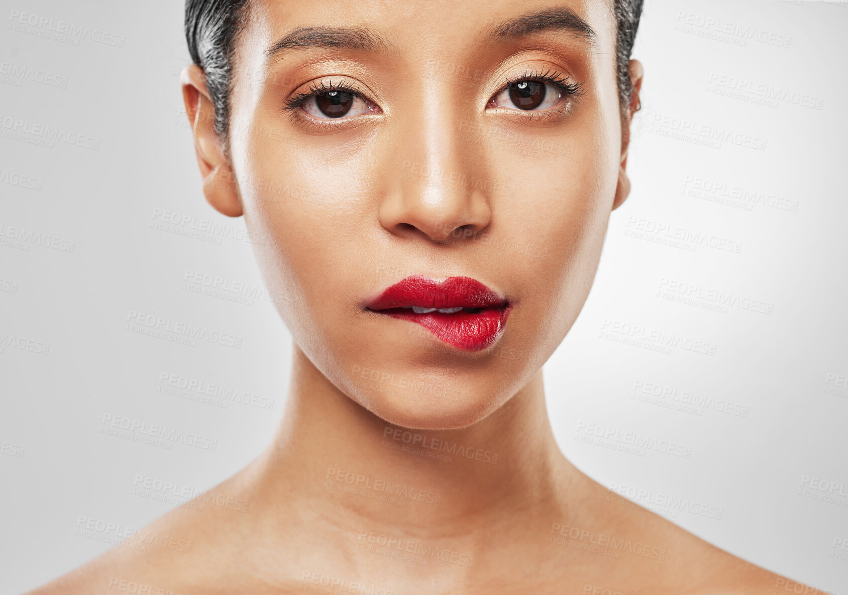 Buy stock photo Studio portrait of an attractive young woman wearing red lipstick and biting her lip against a grey background