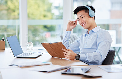 Buy stock photo Shot of a young businessman writing in a notebook while listening to music at work