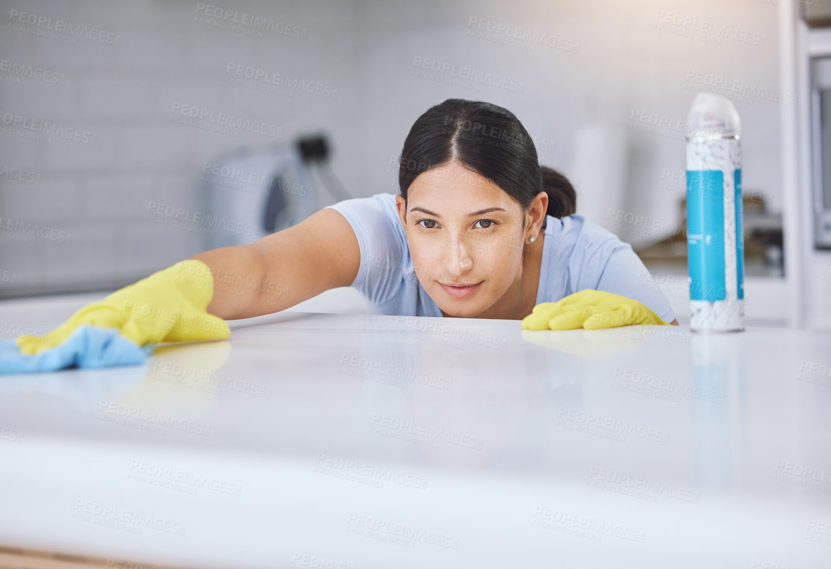 Buy stock photo Shot of a young woman smiling while cleaning a kitchen counter