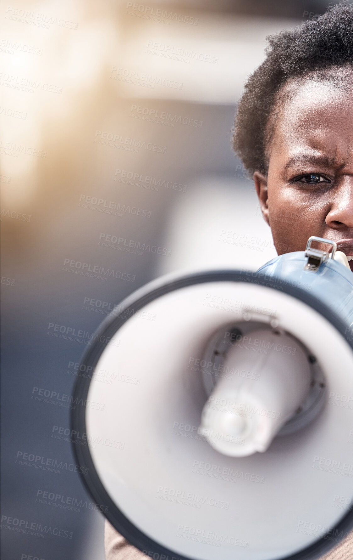 Buy stock photo Shot of a young woman shouting through a megaphone at a protest