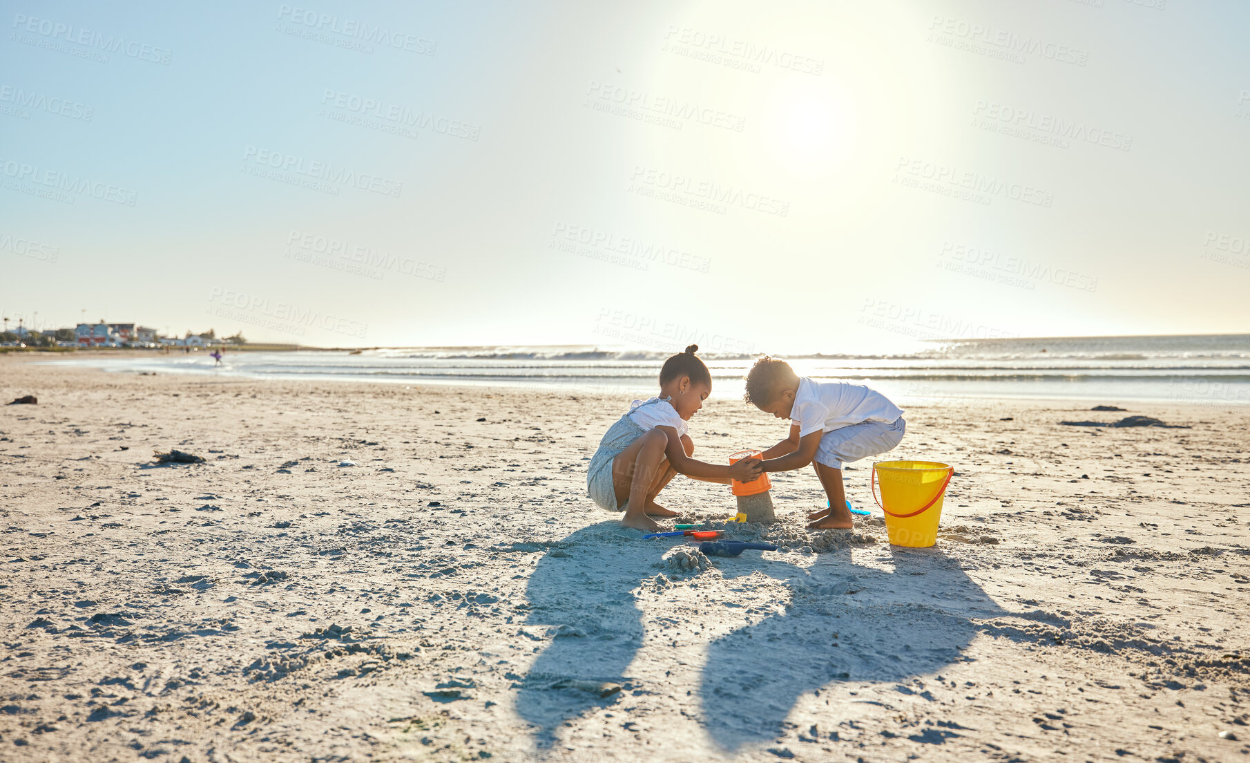 Buy stock photo Boy, girl or sandcastle with bucket, beach or children playing outdoors on vacation in summer. Kids, siblings or plastic toys for building, construction game and holiday for bonding by ocean together