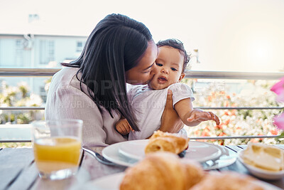 Buy stock photo Shot of a young mother kissing her baby while having lunch at home