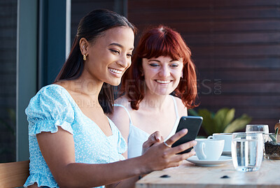 Buy stock photo Shot of two young female friends using a phone together at a cafe