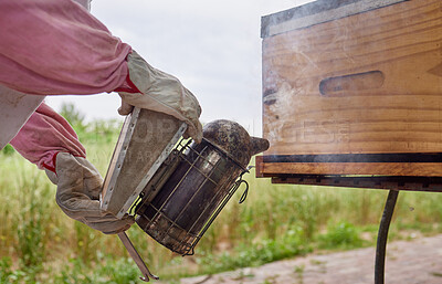 Buy stock photo Shot of a beekeeper using a bee smoker while working on a farm