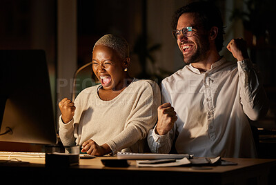 Buy stock photo Shot of two businesspeople cheering while working on a computer in an office at night