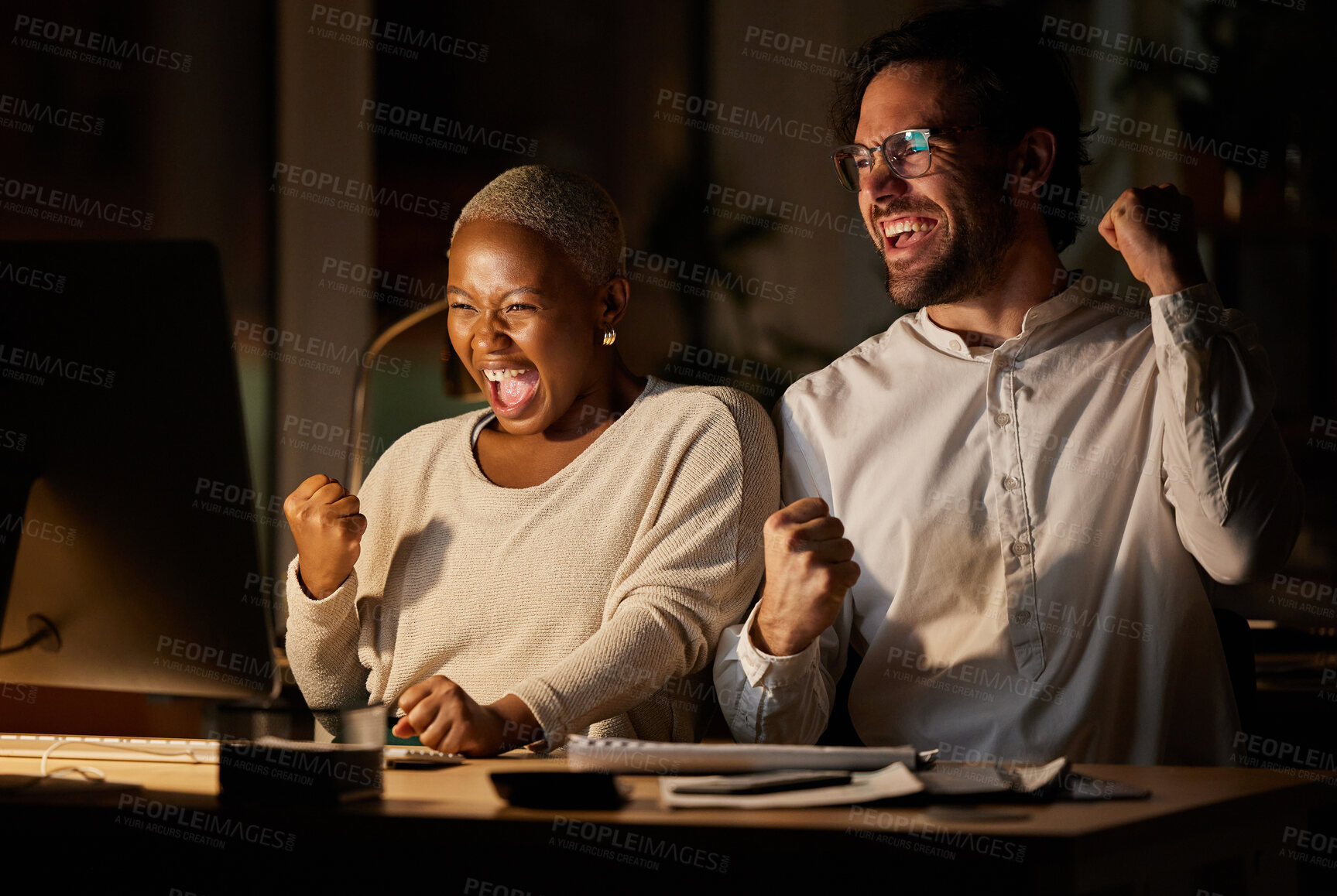 Buy stock photo Shot of two businesspeople cheering while working on a computer in an office at night