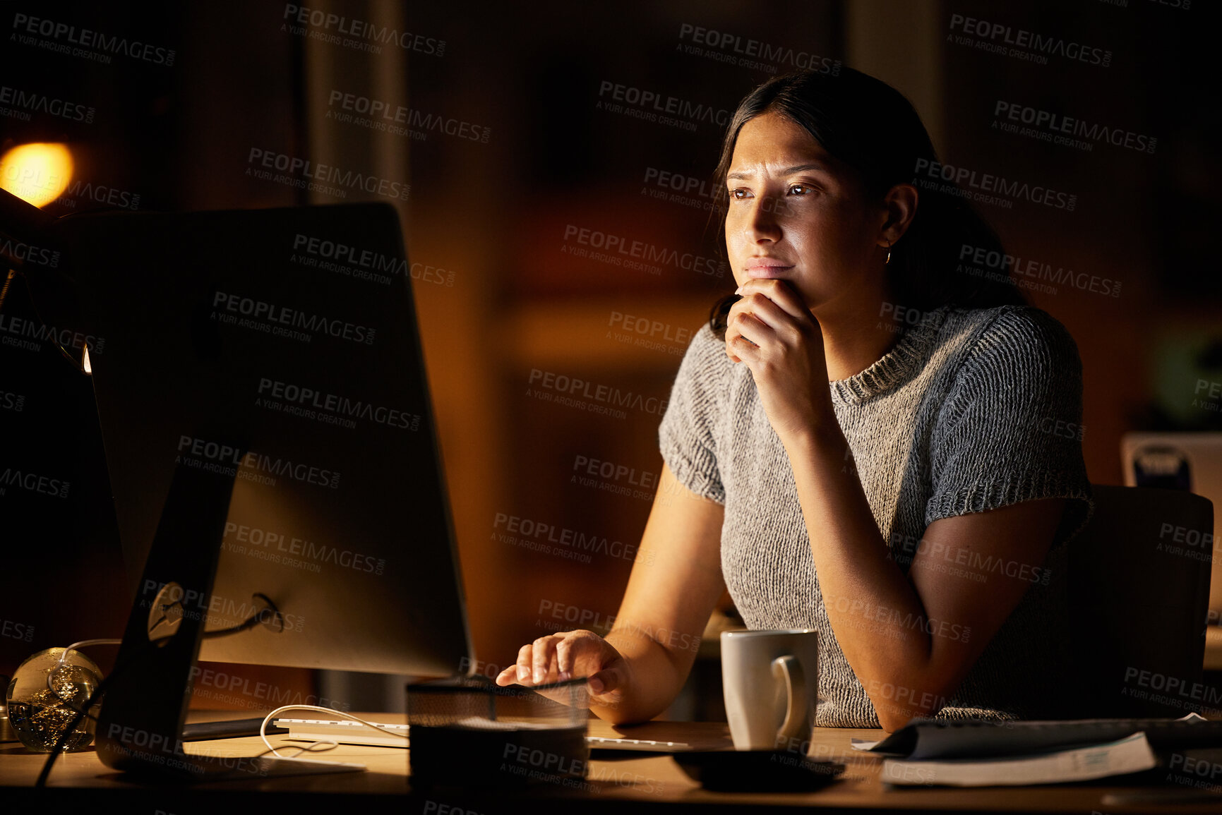 Buy stock photo Shot of a young businesswoman looking thoughtful while working on a computer in an office at night